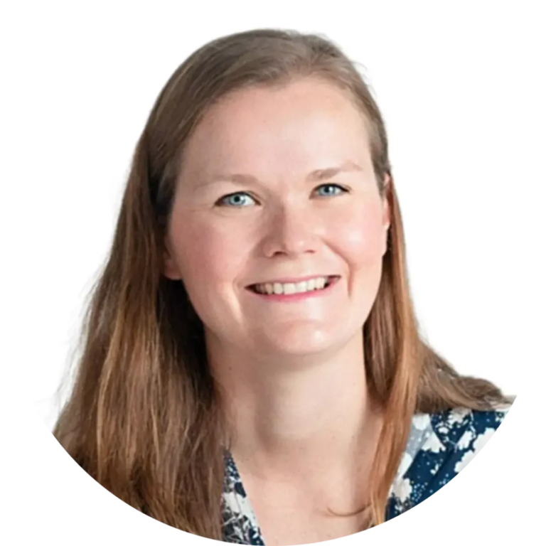 A smiling person with long, light brown hair is pictured in a circular frame. They are wearing a navy blue and white patterned shirt against a white background.