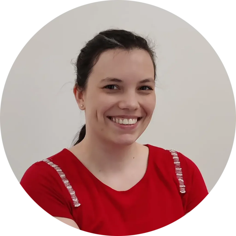 A person with dark hair smiles at the camera, wearing a red shirt with sequin details on the shoulders against a plain white background.
