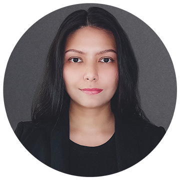 Portrait of a person with long dark hair, wearing a black top and black blazer, against a dark gray background. The image is circular in shape.