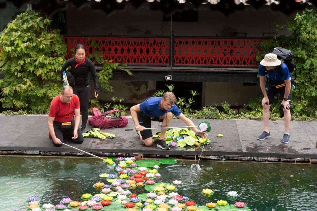 Finding my very own Finest Future in Finland 8 Four people are by a pond, gathering colorful floating lotus flowers using long sticks. They are on a wooden platform, surrounded by greenery and a red railing.