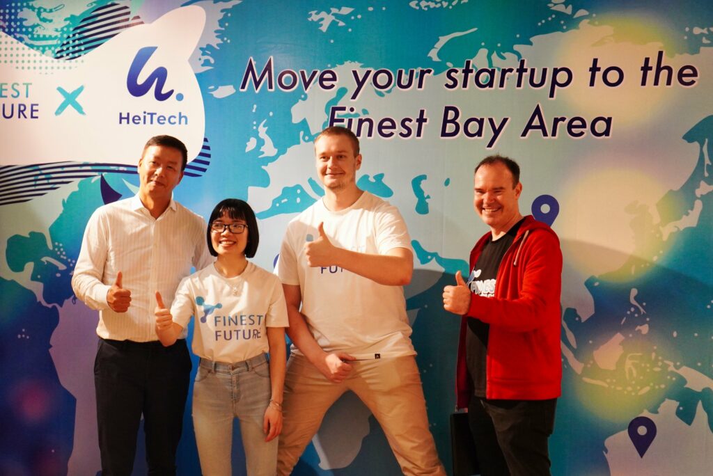 Finest Future’s Delegation Trip to Vietnam - Growth Together, for a Better Future 2 Four people stand smiling and giving thumbs up in front of a colorful backdrop that reads "Move your startup to the Finest Bay Area." Two of them wear T-shirts with the same logo, while the other two wear different attire.